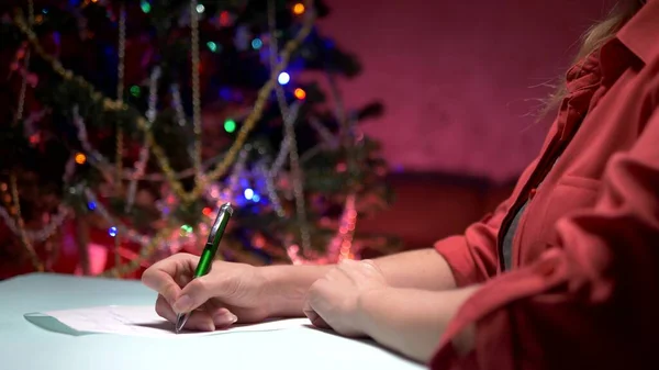 Жінка сидить за столом біля прикрашену ялинку і пише Різдвяний лист Діда Мороза — стокове фото