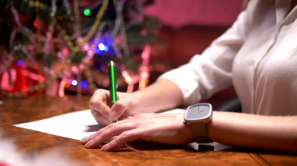 Ділова жінка сидить за столом біля прикрашену ялинку і пише Різдвяний лист Діда Мороза — стокове фото