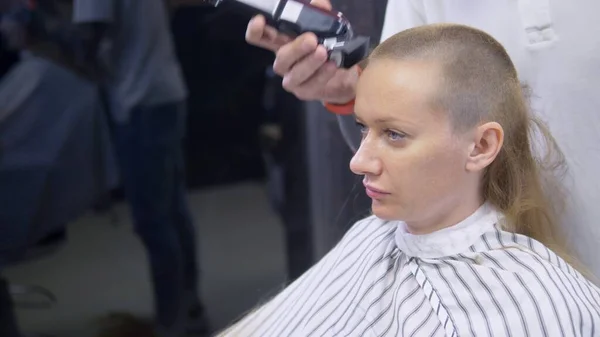 女人光着头剃头。理发师用剪发器剪下女人的长发. — 图库照片