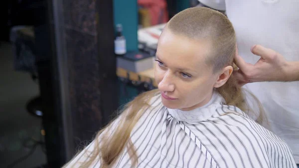 Mulher a rapar a cabeça careca. um cabeleireiro rapa um cabelo longo de mulheres com um cortador de cabelo . — Fotografia de Stock