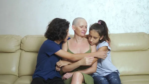 Careca mãe exausta após quimioterapia câncer abraça seus filhos adolescentes sentados em um sofá — Fotografia de Stock