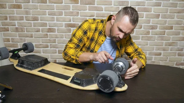 Мужчина-механик чинит электрический скейт, сидящий в мастерской на чердаке. генеральный план — стоковое фото