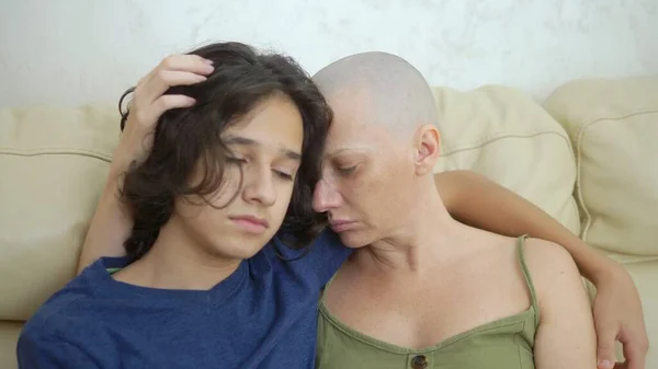 Madre agotada calva después de quimioterapia contra el cáncer abraza a su hijo adolescente sentado en el sofá — Foto de Stock