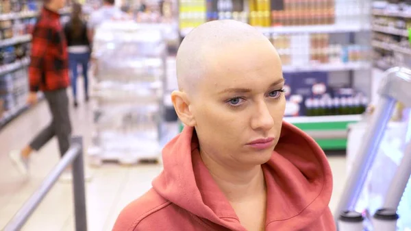 Mujer calva cansada con estilo se para en la tienda. para comprar en el supermercado. pago de las mercancías en la caja . — Foto de Stock