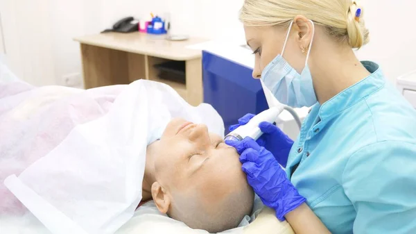 Micronéedle procédure de levage RF. Cosmétologie du matériel. Esthéticienne effectue une procédure de rajeunissement du visage pour une femme chauve . — Photo