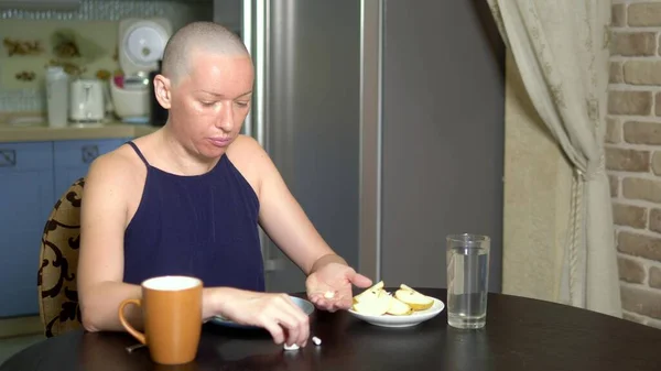 Richtige Ernährung nach Chemotherapie. Eine kahle Frau am Tisch trinkt Pillen beim Essen. — Stockfoto