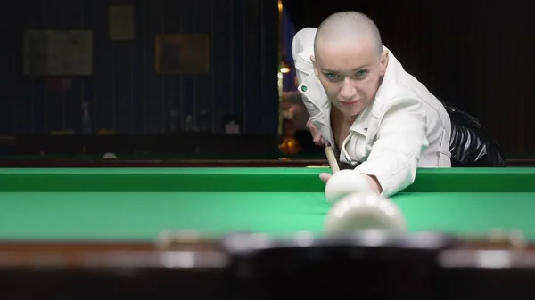 Menina careca elegante em uma jaqueta de couro branco joga bilhar . — Fotografia de Stock