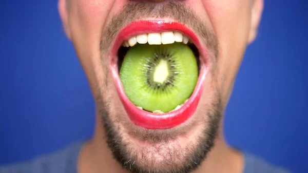 close-up. funny image of a bearded man with lip make-up holding a kiwi in his mouth