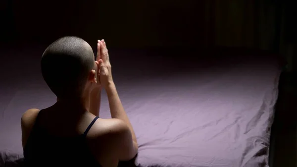 A bald woman prays on her knees by the bed. back view. copy space — Stock Photo, Image