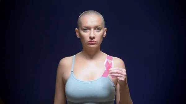 Bald woman against a dark background. healthcare, people and medicine concept - woman holding pink breast cancer awareness ribbon — Stock Photo, Image