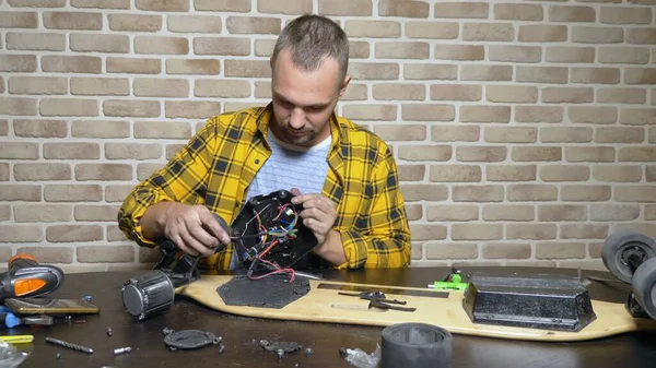 Мужчина-механик чинит электрический скейт, сидящий в мастерской на чердаке. генеральный план — стоковое фото