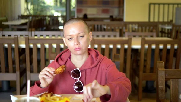 Bald woman eats chicken wings, high-calorie foods and health risks. outdoor cafe. — Stock Photo, Image