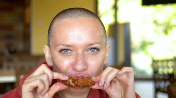 Nahaufnahme. hungrige Frau mit Glatze in einem Restaurant, die leckere Chicken Wings isst. Blick in die Kamera. — Stockfoto