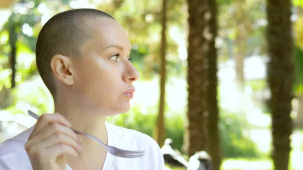 Beautiful young bald woman having lunch at an outdoor cafe. — Stock Photo, Image