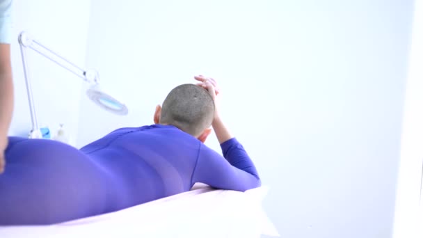 Uma menina careca em um terno roxo recebe um procedimento de massagem lpg . — Vídeo de Stock