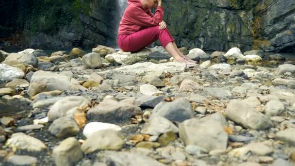 Triste femme chauve assise sur une pierre sur le fond d'une cascade. espace de copie. concept d'unité avec la nature, se cachant des gens . — Video
