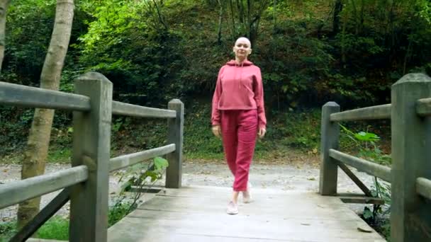 Mujer calva camina sobre un puente de madera en el bosque. El concepto de transición en la vida . — Vídeos de Stock