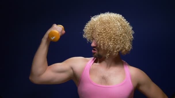 Crazy guy athlete in a wig with dumbbells against a dark background — Stock Video