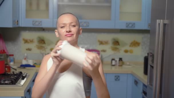 Die glatzköpfige Frau bereitet zu Hause in der Küche Sportnahrung zu. schüttelt einen Cocktail im Shaker — Stockvideo