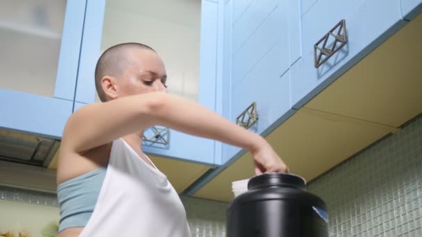 Den skalliga kvinnan förbereder sportnäring hemma i köket. skakar en cocktail i en shaker — Stockvideo
