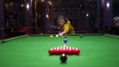 Modaya uygun bir adam bilardo masasına yeşil bir frizle üçgen bir çerçeve içinde tam bir bilardo takımı koyar. Boşluğu kopyala