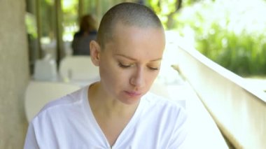 Güzel, genç, kel bir kadın açık bir kafede yemek yiyor..