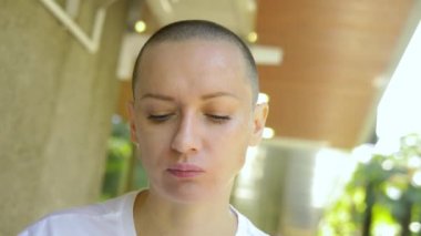 Güzel, genç, kel bir kadın açık bir kafede yemek yiyor..