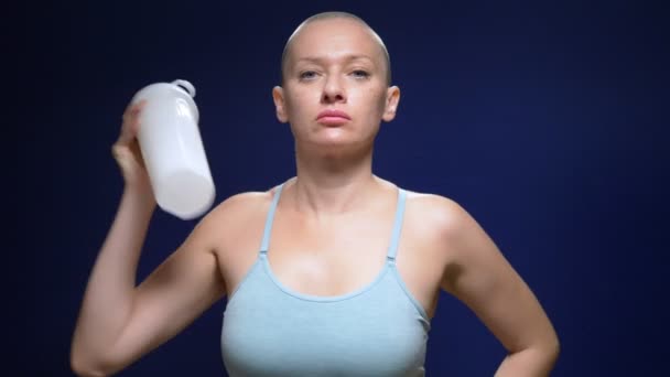Łysa kobieta w sportowym topie potrząsa koktajlem w shakerze na ciemnym tle. — Wideo stockowe