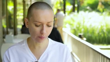 Güzel, genç, kel bir kadın açık bir kafede yemek yiyor..