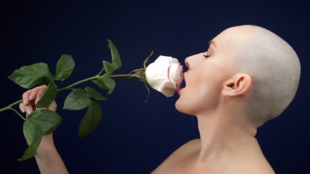 Bela mulher careca em um espartilho de couro preto mantém uma rosa em suas mãos e beija uma flor. aventuras de pessoas estranhas . — Vídeo de Stock