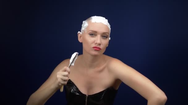 Een vrouw in een leren korset scheert haar hoofd bedekt met scheerschuim met een gevaarlijk scheermes. donkere achtergrond — Stockvideo