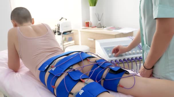 La jeune fille s'allonge sur le canapé et reçoit la procédure de myostimulation sur ses jambes et ses fesses dans un salon de beauté. Soins du corps, perte de poids . — Video