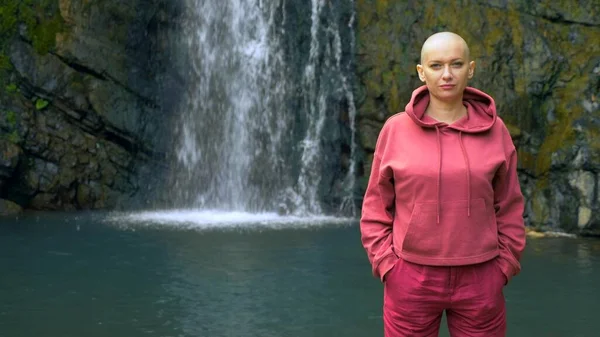 Mooie kale vrouw die naar de camera kijkt, staande op de achtergrond van een waterval. concept van vrijheid, overwinning, doel bereiken. kopieerruimte — Stockfoto