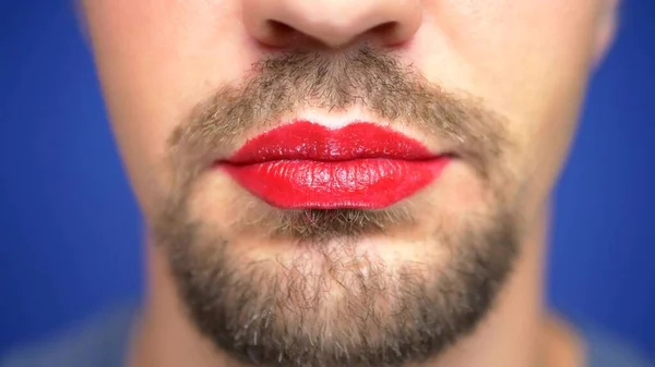 Primer plano. Un hombre barbudo con los labios pintados sonríe sexualmente y sopla un beso . — Foto de Stock