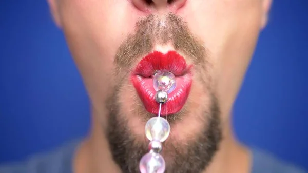 close-up. funny bearded man with lip makeup pulls beads from his mouth