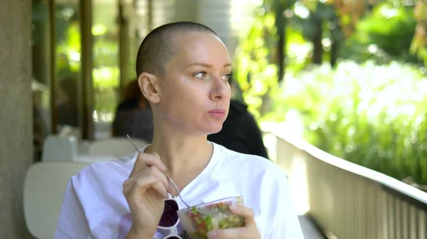 Beautiful young bald woman having lunch at an outdoor cafe.