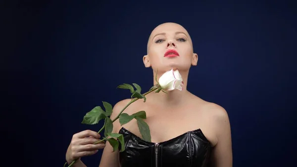 Mooie kale vrouw in een zwart lederen korset houdt een roze roos in haar handen en kust een bloem. avonturen van vreemde mensen. — Stockfoto