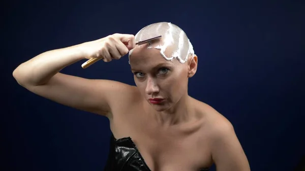 Μια γυναίκα με δερμάτινο κορσέ ξυρίζει το κεφάλι της καλυμμένο με αφρό ξυρίσματος με επικίνδυνο ξυράφι. σκούρο φόντο — Φωτογραφία Αρχείου