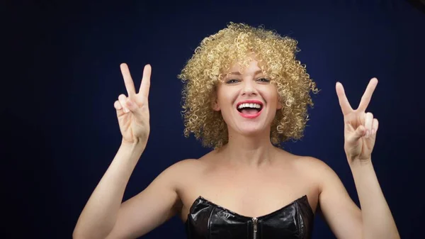 Naughty woman with short white curly hair in a black leather corset shows a sign of Victoria, victory. two fingers up. emotions and gestures. copy space — Stock Photo, Image
