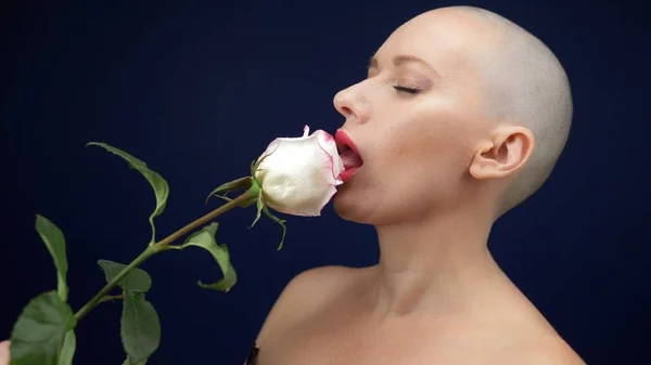 Die schöne, glatzköpfige Frau im schwarzen Lederkorsett hält eine rosa Rose in den Händen und küsst eine Blume. Abenteuer fremder Menschen. — Stockfoto