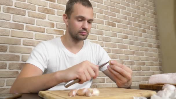 Ένας άνθρωπος ξεφλουδίζει σκόρδο κάθεται σε ένα τραπέζι σε ένα φόντο ενός τοίχου από τούβλα. — Αρχείο Βίντεο