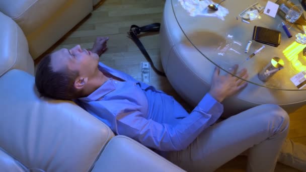 Un joven experimenta alucinaciones por consumir drogas y alcohol mientras está acostado en el suelo junto a una mesa en la sala de estar . — Vídeos de Stock