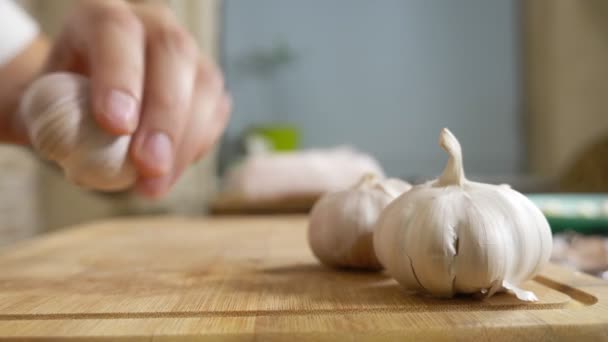 Closeup κεφάλι του σκόρδου, αρσενικά χέρια ξεφλουδίσει το σκόρδο σε μια ξύλινη σανίδα — Αρχείο Βίντεο