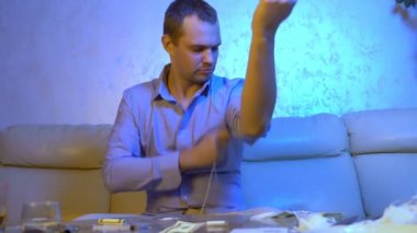 Genç işadamı oturma odasındaki kanepede alkol ve uyuşturucu dolu bir masada otururken kendine uyuşturucu enjekte ediyor.