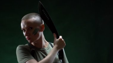 Kamuflaj makyajlı kızgın kel kız siyah arka planda pala kılı traş ediyor.