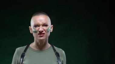 Kamuflaj makyajlı vahşi kel kadın elinde beyaz bir masaj aleti tutuyor.