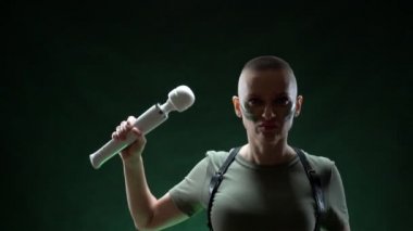 Kamuflaj makyajlı vahşi kel kadın elinde beyaz bir masaj aleti tutuyor.