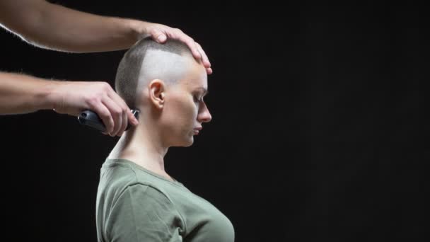 Koncepció katonai lány. Egy férfi fodrász kezei borotválják egy nő fejét kopaszra, katonai frizurával. Fekete háttér — Stock videók