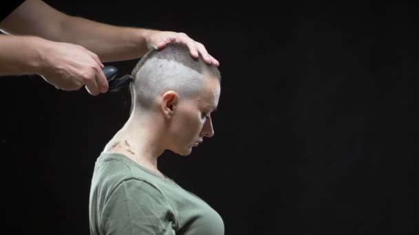 Concetto ragazza militare. le mani di un parrucchiere uomo radono una testa di donne calva, acconciatura militare. Fondo nero — Video Stock