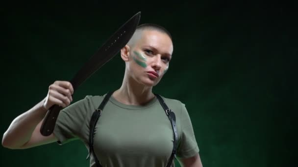 Chica calva enojada con maquillaje de camuflaje afeitar el pelo machete sobre un fondo negro — Vídeo de stock